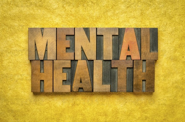 Mental health word abstract in vintage letterpress wood type printing blocks against yellow textured bark paper, wellbeing and healthcare concept