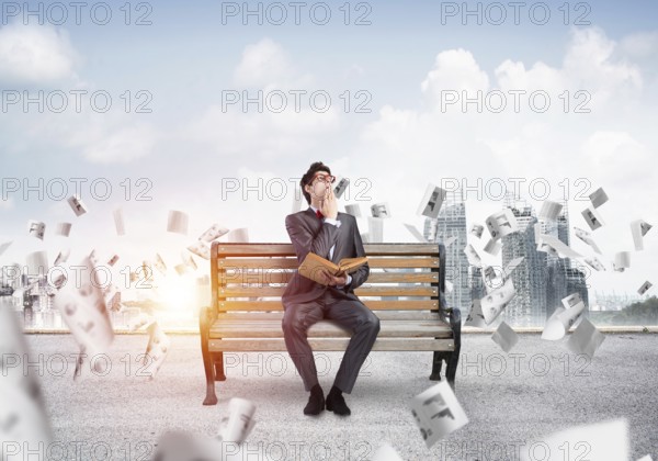 Young student with a book on the bench, flying around in the chaos of paper
