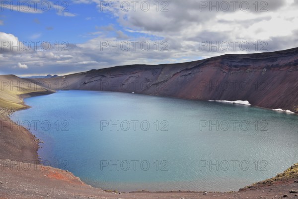 Oval blue lake in the crater of the volcano cooled down. Steep banks of the lake of red rhyolite. Iceland in July
