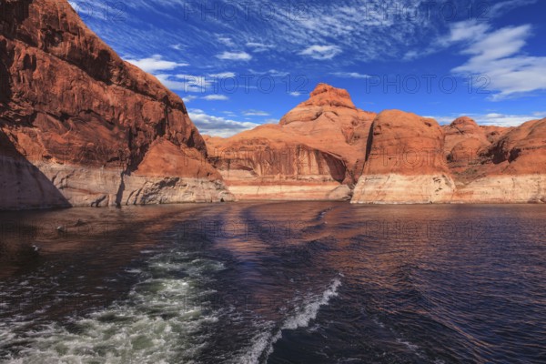 The foamy trace from powerboat crosses emerald waters. Hills from red sandstone surround the lake. The lake Powell on river Colorado