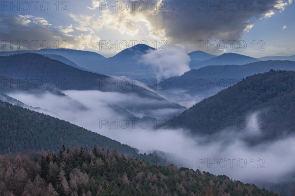 Landscape shot with cloudy sky and fog in the valley. View from a rock in the middle of forest and nature. Viewpoint in the morning in the Palatinate Forest, Germany, Europe