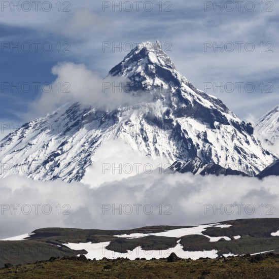 Beautiful mountain landscape of Kamchatka Peninsula: scenery view on steep slope cone of Kamen Volcano (Stone Volcano) and clouds with blue sky. Russian Far East, Kamchatka Region, Klyuchevskaya Group of Volcanoes