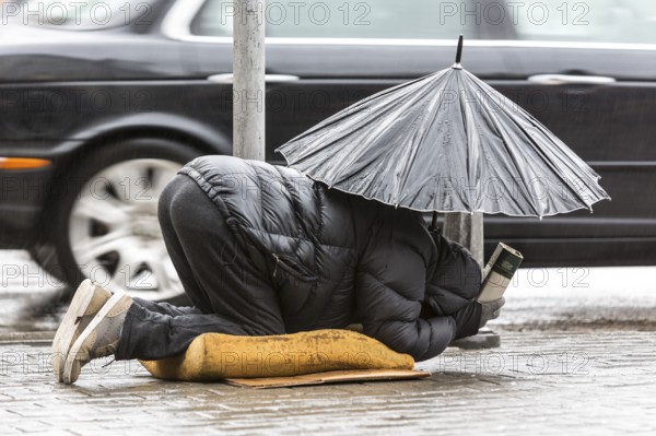 Homeless beggar is begging for money in a main street in Sofia holding an umbrella in a rainy day. Bulgaria is the poorest country in EU