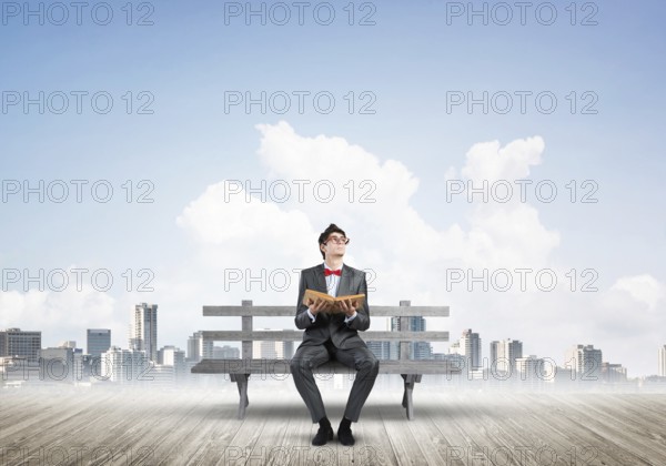 Student sits on a bench, holding a book. Traditional education concept