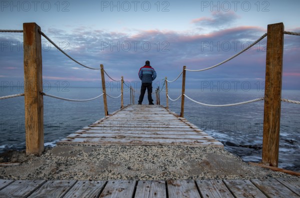 Person standing at the edge of a wooden pier in the sea at sunrise, People active outdoors enjoy ocean. Protaras Cyprus