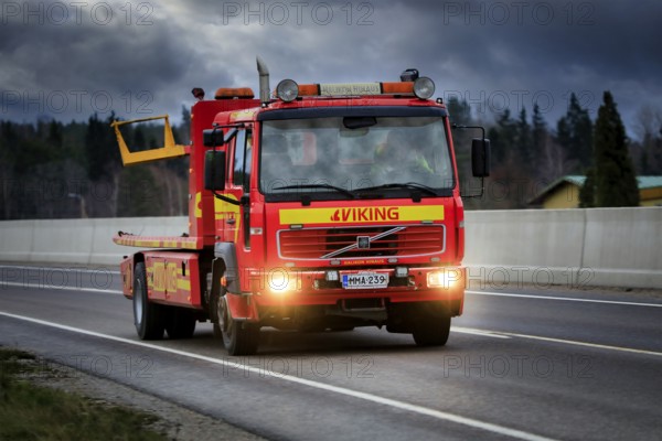Volvo tow truck of Halikon Hinaus driving along Highway 52 under dramatic sky on a dark winter evening. Salo, Finland. December 28, 2020