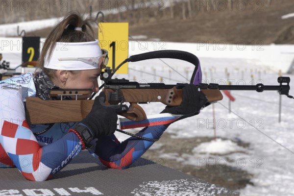 Sportswoman biathlete aiming, rifle shooting prone position. Biathlete Victoria Petrova Saint Petersburg in shooting range. Junior biathlon competitions East of Cup. Kamchatka, Russia, April 14, 2019, Europe