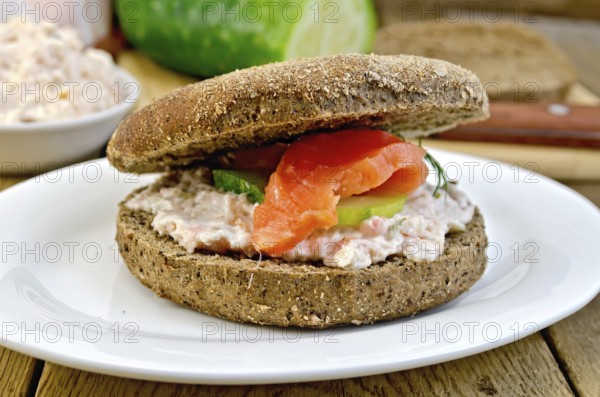 Sandwich of rye bread with cream, cucumber, dill and salmon on a plate on a wooden boards background