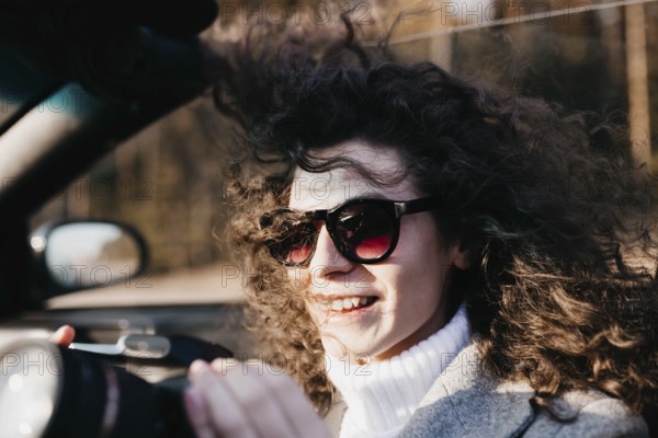 The woman with sunglasses and curly hair is cheerful, holding a camera in sunlight