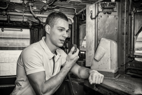 Black and White Retro Close Up of Young Man Speaking into Handheld Radio in Engine of Old Fashioned Train Locomotive