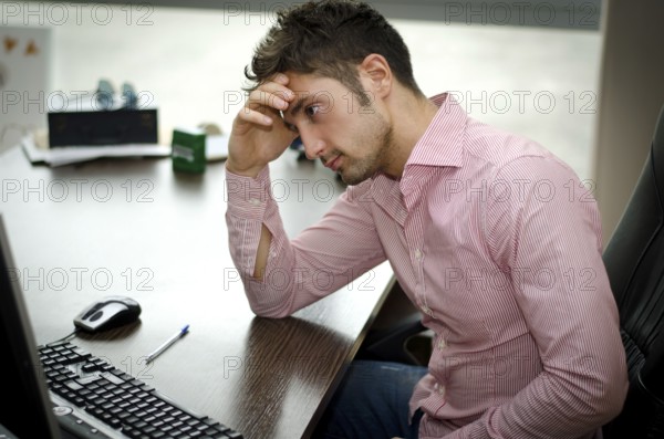 Preoccupied, worried young male worker staring at computer screen in his office