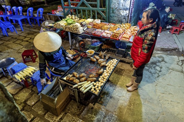 A busy street market with a stall selling grilled food surrounded by visitors, restaurant in the streets of Sa Pa in Vietnam