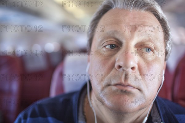 Close-up shot of mature man listening to music in headphones during traveling by plane. He looking distracted