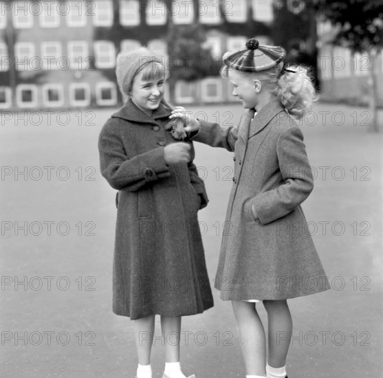 Girls in the 1950s. Two teenage girls dressed in outfits typical of the decade. Both in warm coats standing outside the school building on the schoolyard. 1954. Conard ref 2722