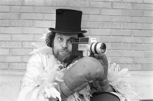 In the 1970s. A man is filming with a amateur film camera. The film was then developed and shown on a film projector on a fold up screen at home. Ricky Bruch (1946-2011) Swedish track and field athlete. He was known for being somewhat of a showman pictured here wearing boxing gloves, a feather boa and a cylinder hat. 1975