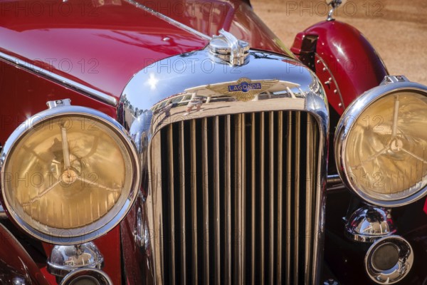 Lisbon, Portugal - Sep 29, 2024: Close view of front grille, headlights and hood of vintage red Lagonda LG45 on sunny day. Selective focus, logo and badge of luxury sports car of 1930s, 2-door drophead coupe version, Lagonda, UK