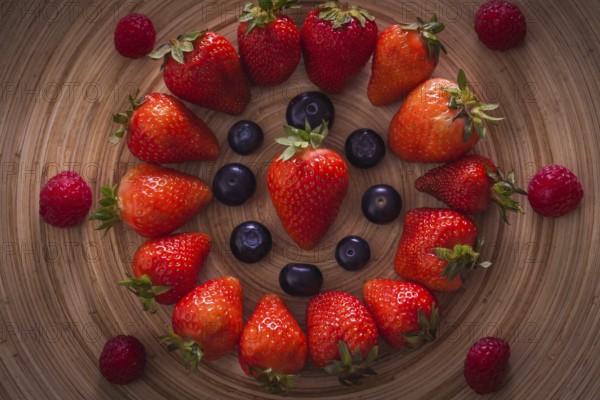 Red strawberries lie in a circle on a wooden plate with blueberries