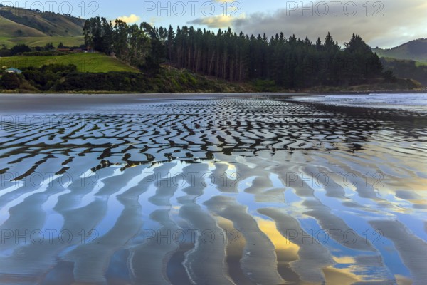 The sandy ripples of the beach reflect the clouds. Incredible sunset on the Pacific coast, New Zealand. The concept of active and ecotourism