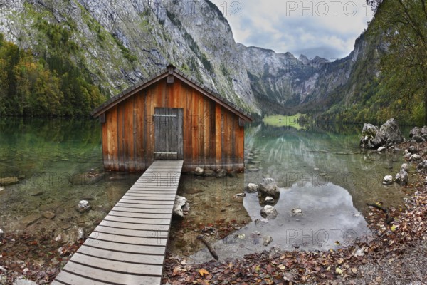 Cloudy day at Lake Koenigssee. Boathouse connected to the coast wooden decking. Clouds and mountains reflected in the water