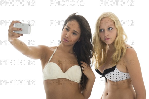 Black and white girl friends in bikini at the beach making selfie