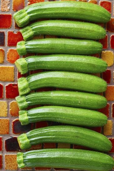 Mini zucchini vegetables in a row on red brown tiles table