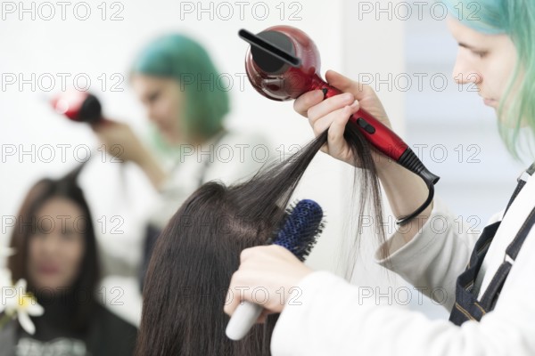 Female hairstylist dries brunette hair with red hair dryer and blue hairbrush in professional beauty salon