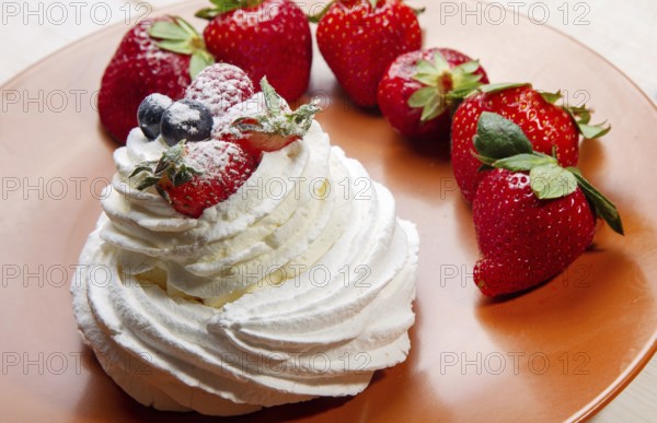 Meringue cake decorated with berries on top on brown plate