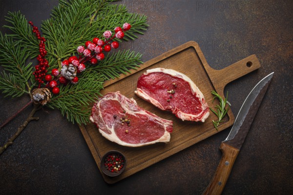 Two raw uncooked meat beef steaks on wooden cutting board with knife and seasonings on dark rustic background with Christmas festive decoration from above, food photography