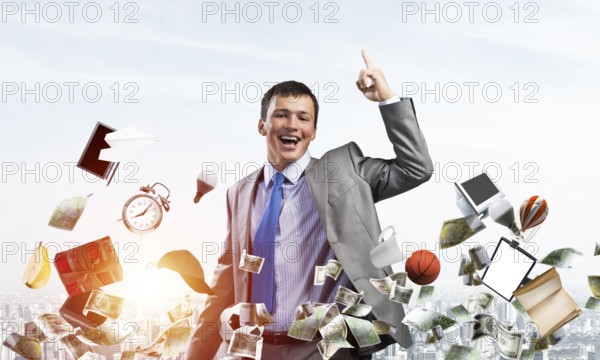 Young businessman and falling from sky various goods and cash. Handsome man in business suit and tie on blue sky background. Ambitions and creativity in business. Retail advertising of discount offer