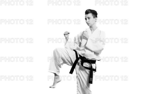 Girl in karate suit kimono in studio at grey background. Female child shows judo or karate stans in white uniform with black belt. Individual martial art sport . Full body portrait