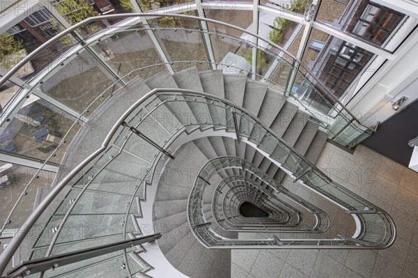 A modern spiral staircase with glass railings and a triangular shape in a bright room, Free and Hanseatic City of Hamburg, Germany, Europe