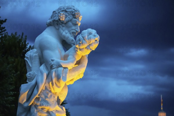 Marble statue of a man holding a small child at the castle in Karlsruhe beautiful lightened in the evening. Sculpure of a strong man holding a small child at the castle in Karlsruhe beautiful lightened in the evening