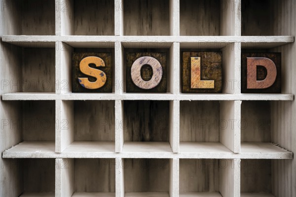 The word SOLD written in vintage ink stained wooden letterpress type in a partitioned printer's drawer