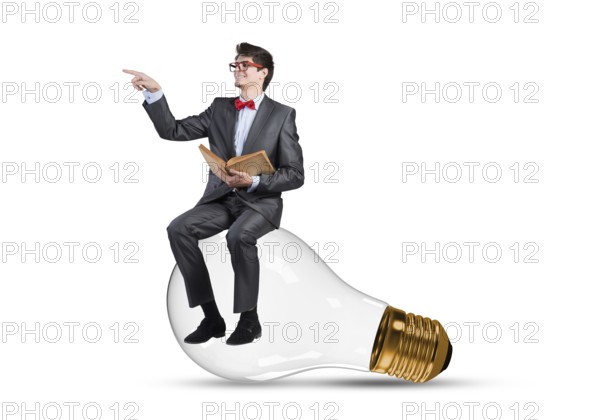 Young businessman sits on an electric light bulb. holds a book in his hands