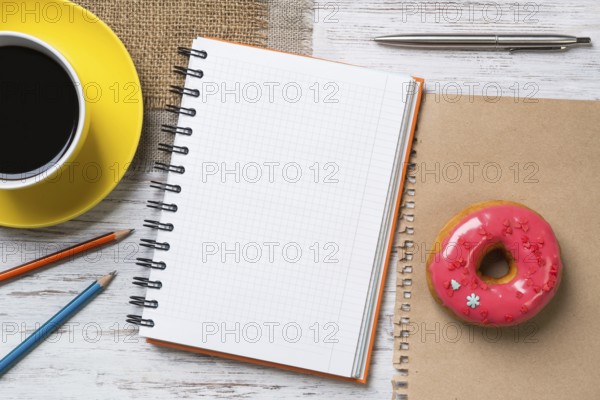 Opened notepad and cup of coffee with donut on wooden table