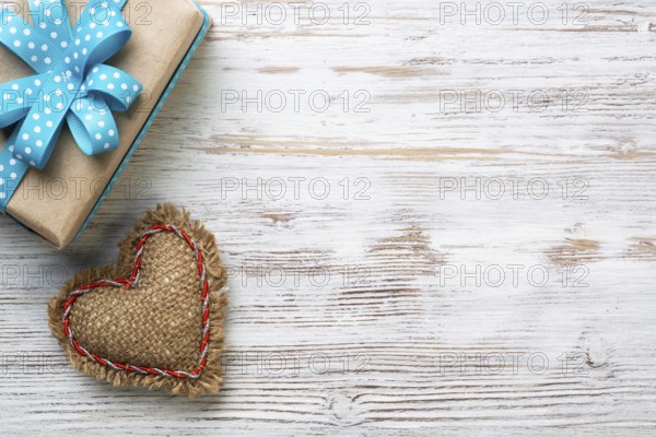 Flat lay cute composition with handmade fabric heart. Gift box with ribbon bow on wooden table. Happy birthday or anniversary congratulation. Romantic message template with copy space