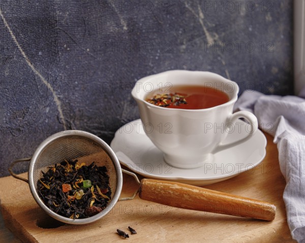 White ceramic tea cup and strainer with tea leaves on wooden board on windowsill, copy space