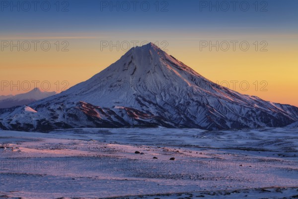 Stunning winter mountain landscape of Kamchatka Peninsula, beautiful morning snow capped cone of volcano at sunrise, full daylight arrives and scenery yellow-blue sky on horizon. Russian Far East