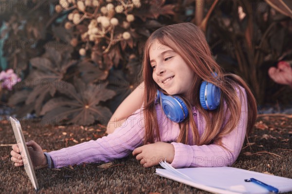 Blond kid girl selfie photo with tablet pc lying on grass turf with headphones