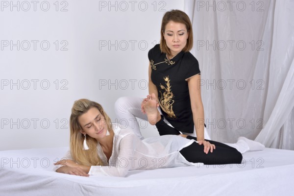 Thai massage. Massage therapist works with patient and massages her body. Studio shot