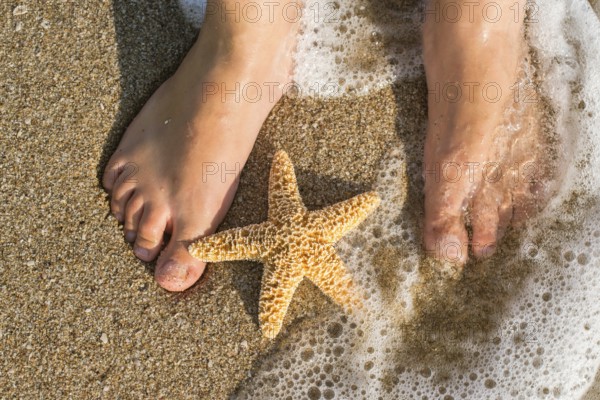 Starfish and feet on the beach. Sea waves