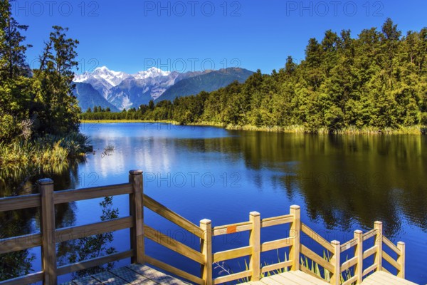 Magnificent snow-capped mountains and forests surround the Lake Matheson. Mirror glacial lake Lake Matheson is surrounded by mountains Steps go down to the water