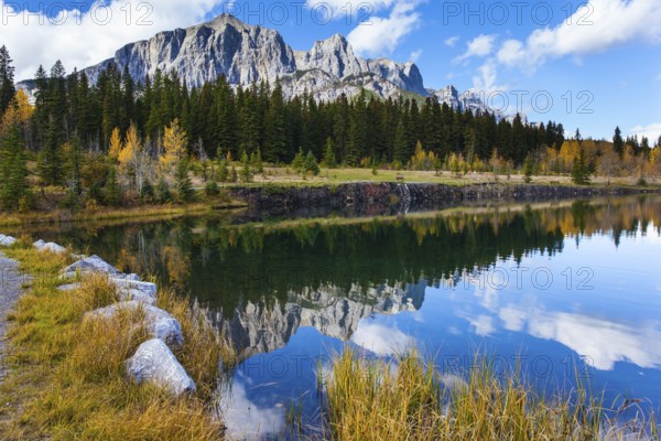 Bright autumn forest is reflected in the smooth water of the lake. The city of Canmore. Three Sisters Mountain in Canadian Banff Park. The concept of active, ecological and photo tourism