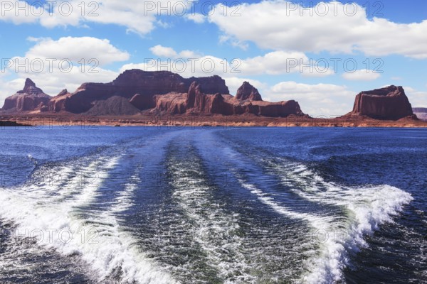 Foamy trace of a motor boat crosses the emerald waters. In distance the coast of red sandstone. Lake Powell on the Colorado River