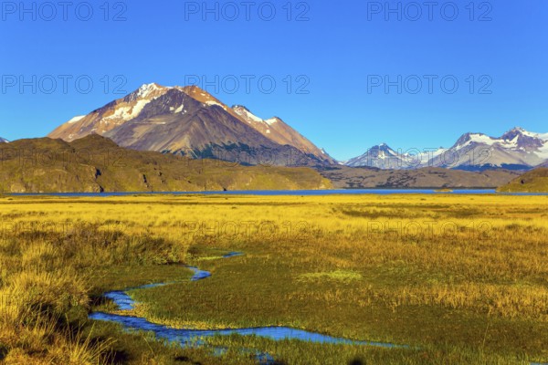 The yellow grass field with streams from underground sources. Trip to the Argentine Patagonia. The private hacienda are surrounded by distant mountains. The concept of exotic and active tourism