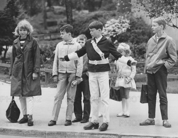Junior safety patrol in the 1960s. A teenage boy stands with his arms out and signals to the pedestrians to stop at the crosswalk. When the cars have passed or stopped, the children can walk across the street. Being part of the Junior safety patrol was voluntary for the school students and the reward was sometimes to go on shorter trips and excursions. Nowadays, the operation is closed in many municipalities. Sweden 1964