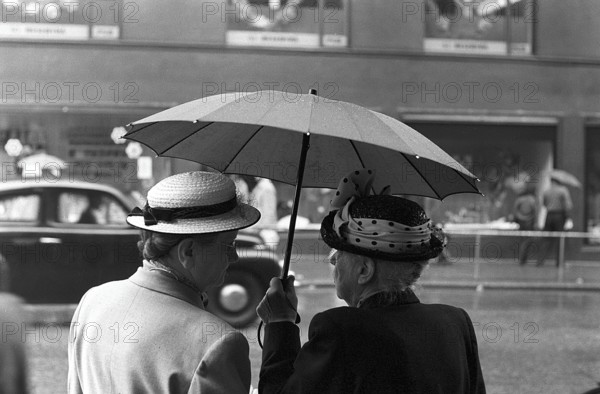 Umbrellas in the 1950s. The rain is pouring and two elderly ladies is seen holding an umbrella over themselves. It's a rainy day in Stockholm Sweden 1953. ref 1, 2