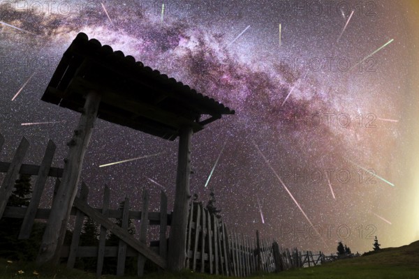 A view of a Meteor Shower and the purple Milky Way with wooden entrance door with a roof and fence silhouette in the foreground. Night sky nature summer landscape. Perseid Meteor Shower observation. Colorful shooting stars