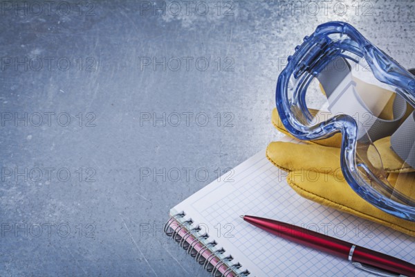 Plastic goggles leather gloves copybook pen on metallic background