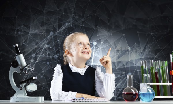 Little girl scientist sitting at desk in elementary science class. Research and education in school. Chemical laboratory with microscope, flasks and test tubes. Happy schoolgirl finger pointing up